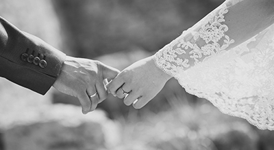 Close up of a man in a suit and woman in a wedding dress holding hands (black and white)