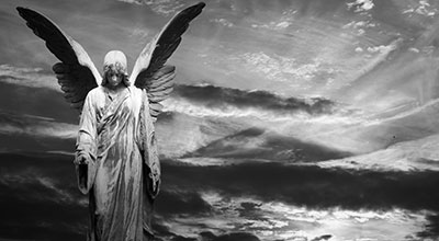 Statue of an angel with spreading wings with a sunset in the background (black and white)