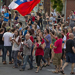 Des manifestants, vêtus de rouge, frappent sur des casseroles. Un drapeau du Québec et un drapeau rouge flottent au-dessus.