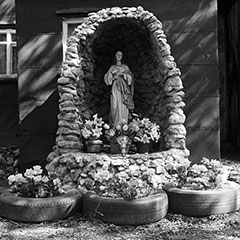 A stone Marian niche intended for the Virgin Mary is found in front of a house. Flowers are placed near the statue.