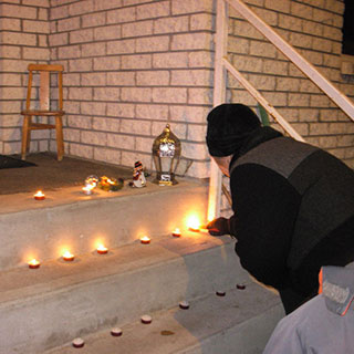 A man lights candles placed on the steps in front of a house.