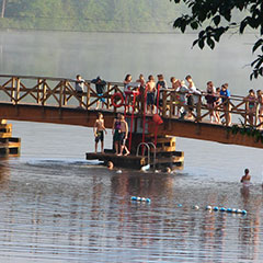 Children playing on a bridge to which a ladder is attached, allowing them to swim in the lake.