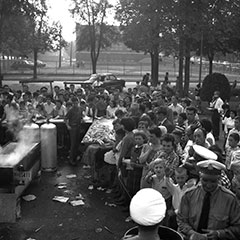 Des gens sont assemblés lors d'une épluchette de blé d'inde dans un parc. Un réservoir d'eau bouillante est visible.